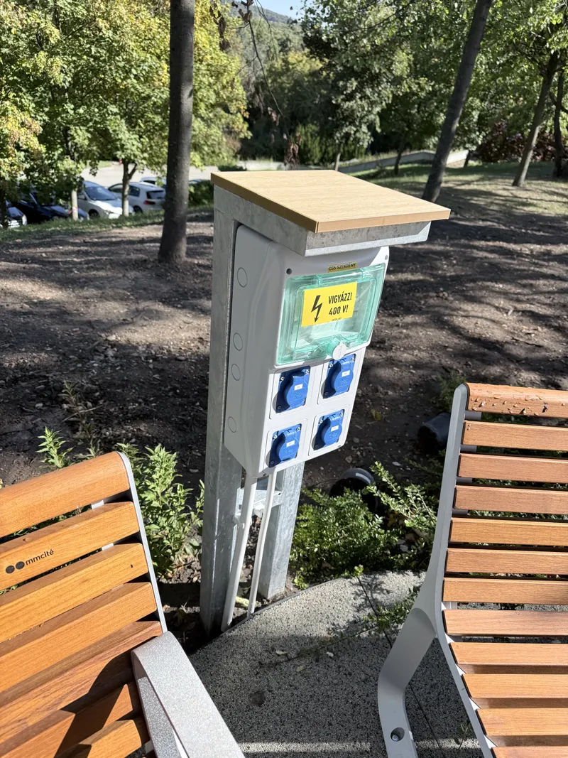 Kültéri áramvételi oszlop négy kék ipari dugaljjal parkos környezetben
