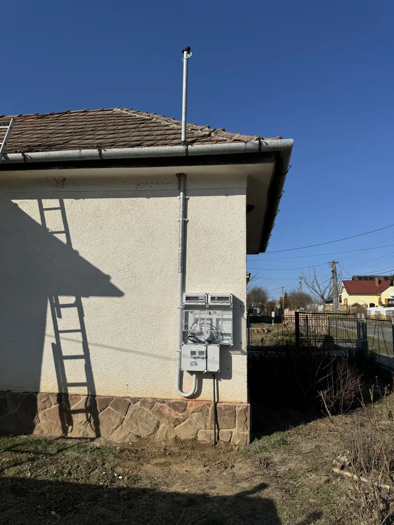 Házfalra szerelt fogyasztásmérő szekrény és tetőn átvezetett felvezető cső