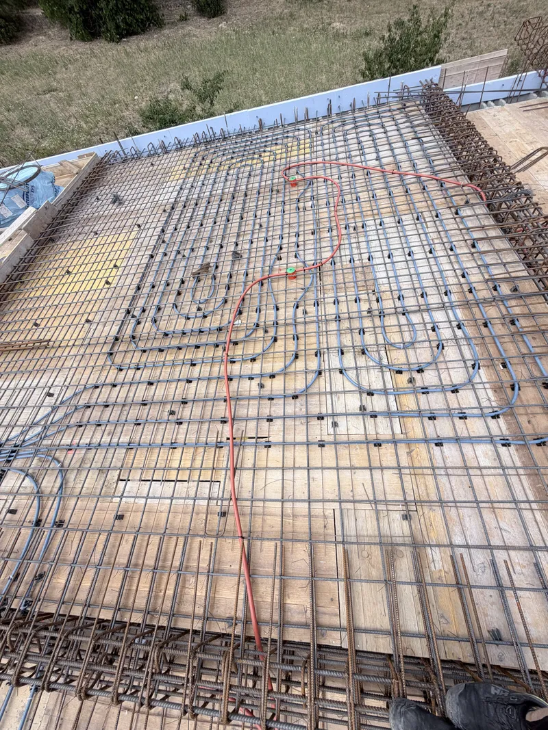 Betonvas hálóra kötözött padlófűtés-hurkok és kék védőcsövek födémen